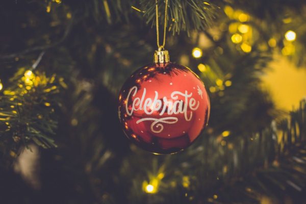 Red Christmas ornament with "Celebrate" text hanging on a tree with soft background lights.