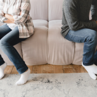 A couple sitting on opposite ends of a sofa with arms crossed during a conflict.