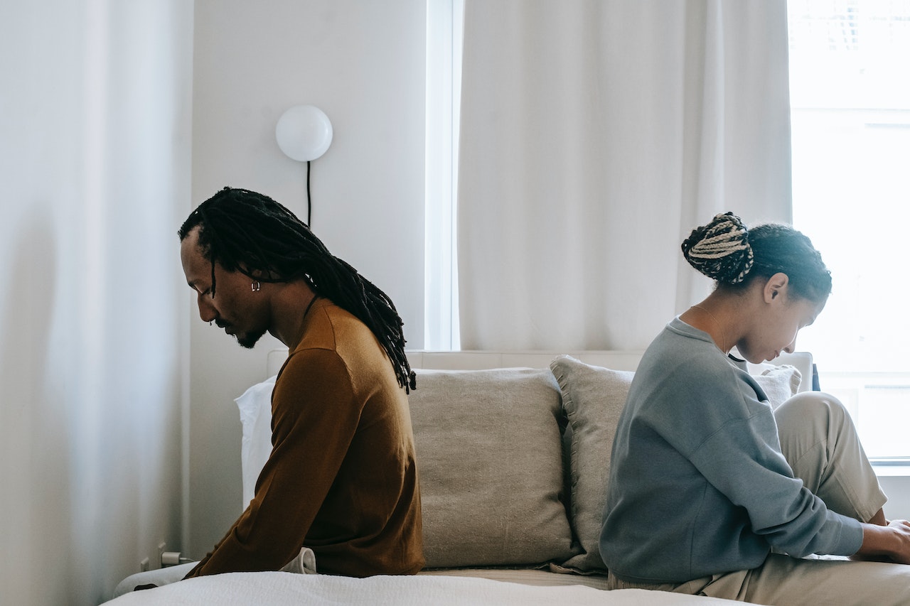 Sad couple sitting back to back on a bed facing away during a conflict