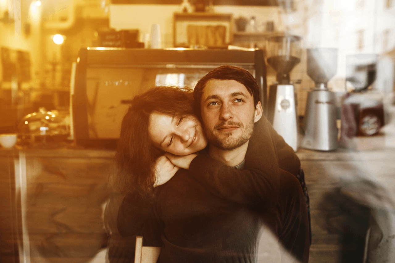 A man and woman sitting at a cafe table enjoying coffee and smiling at each other.
