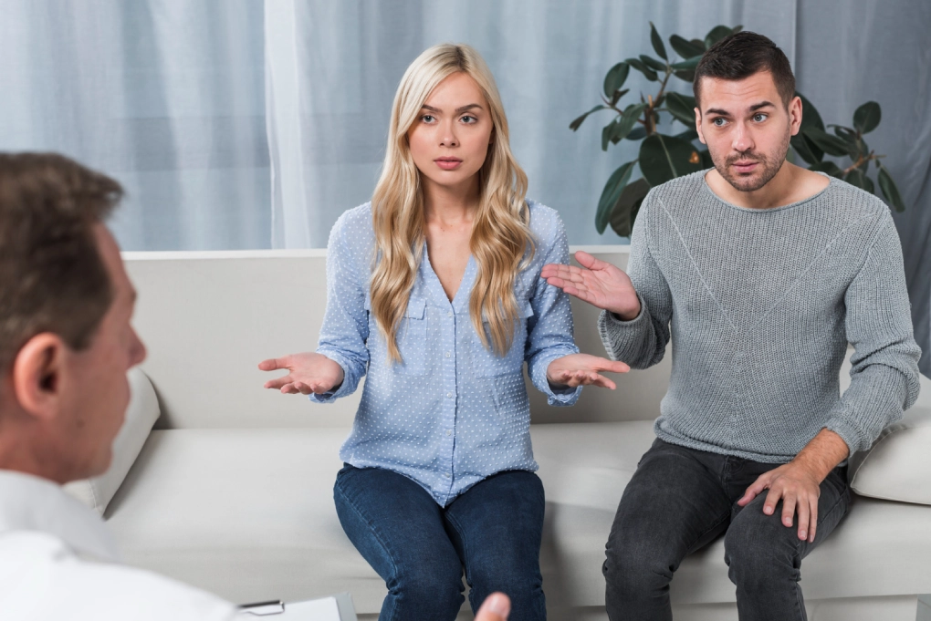 Frustrated couple gesturing with open hands while speaking with a therapist during a couples counseling session