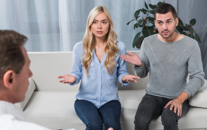 Frustrated couple gesturing with open hands while speaking with a therapist during a couples counseling session