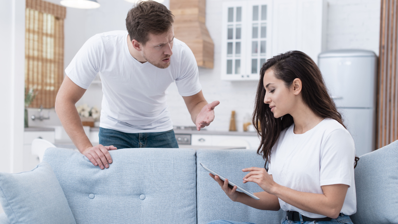 An angry man arguing while a woman ignores him using a tablet.