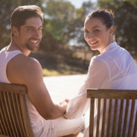 A smiling couple sitting outdoors together on wooden chairs during a retreat getaway.