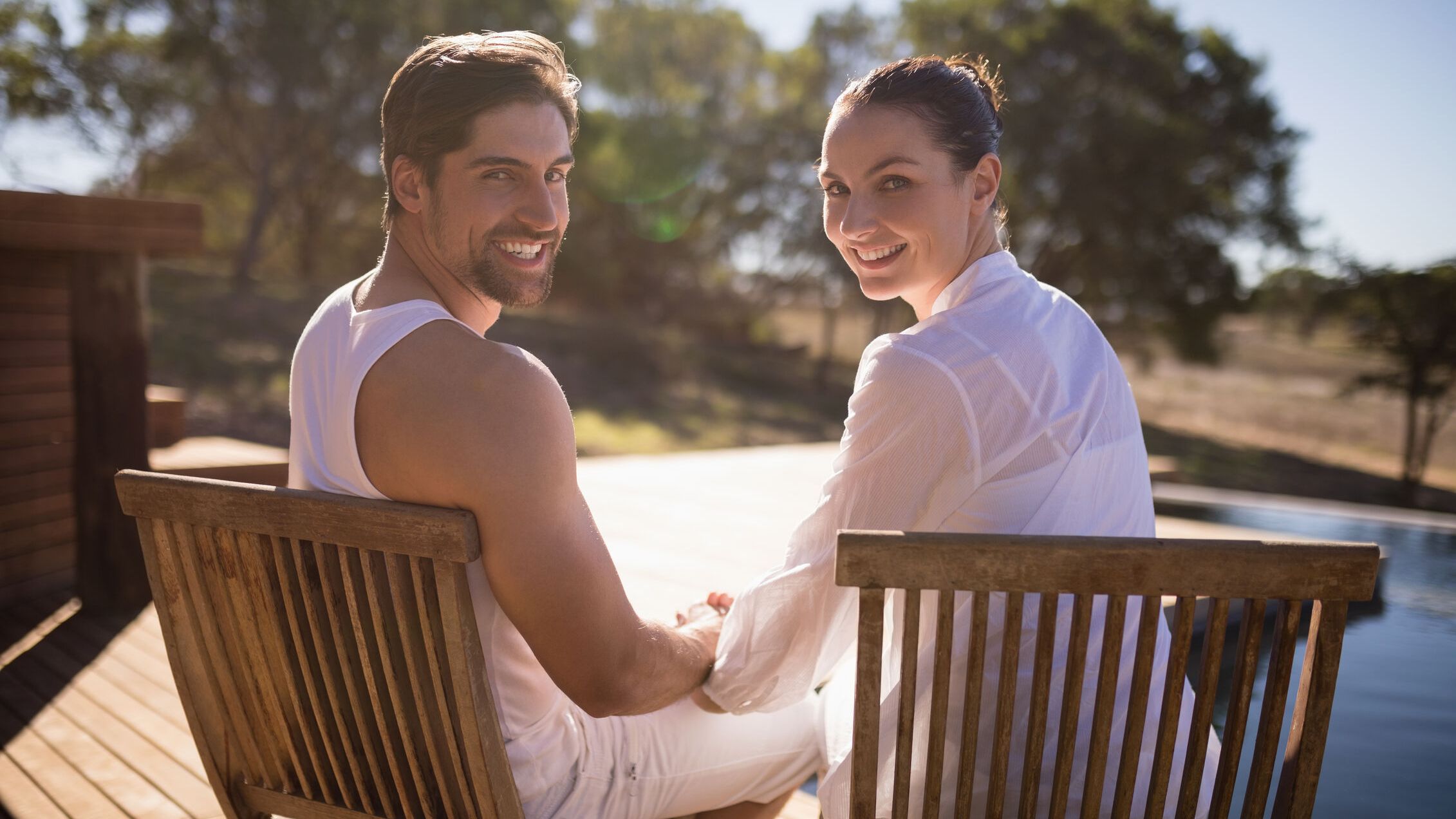 A smiling couple sitting outdoors together on wooden chairs during a retreat getaway.