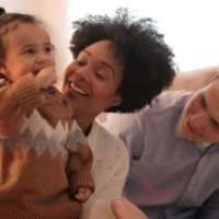 Smiling parents playing happily with their young child at home, creating strong family bonds.