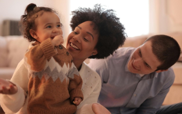 Smiling parents playing happily with their young child at home, creating strong family bonds.