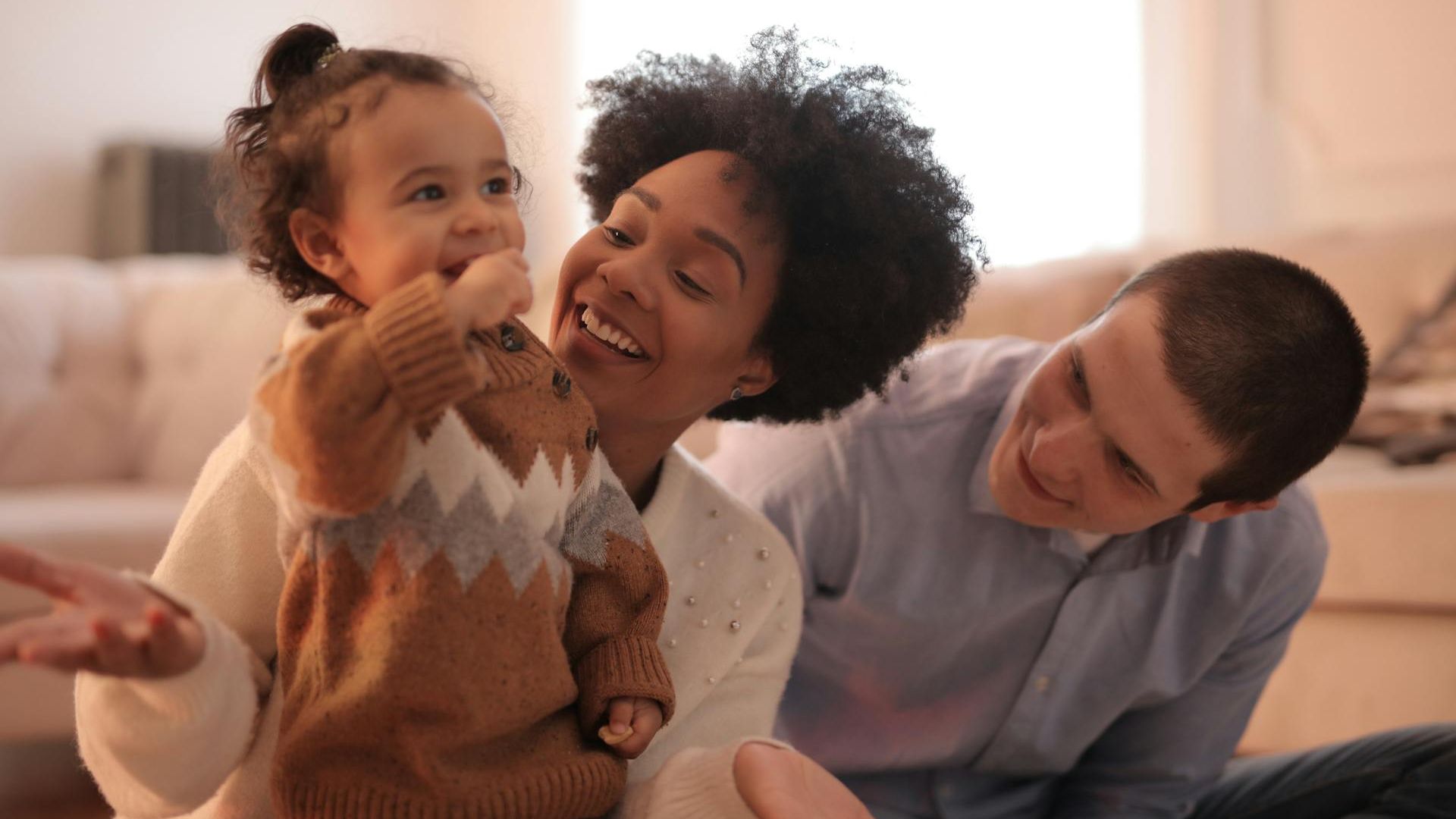 Smiling parents playing happily with their young child at home, creating strong family bonds.