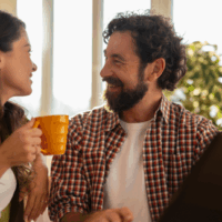 Smiling bearded man looking at his partner holding a yellow mug during a conversation.