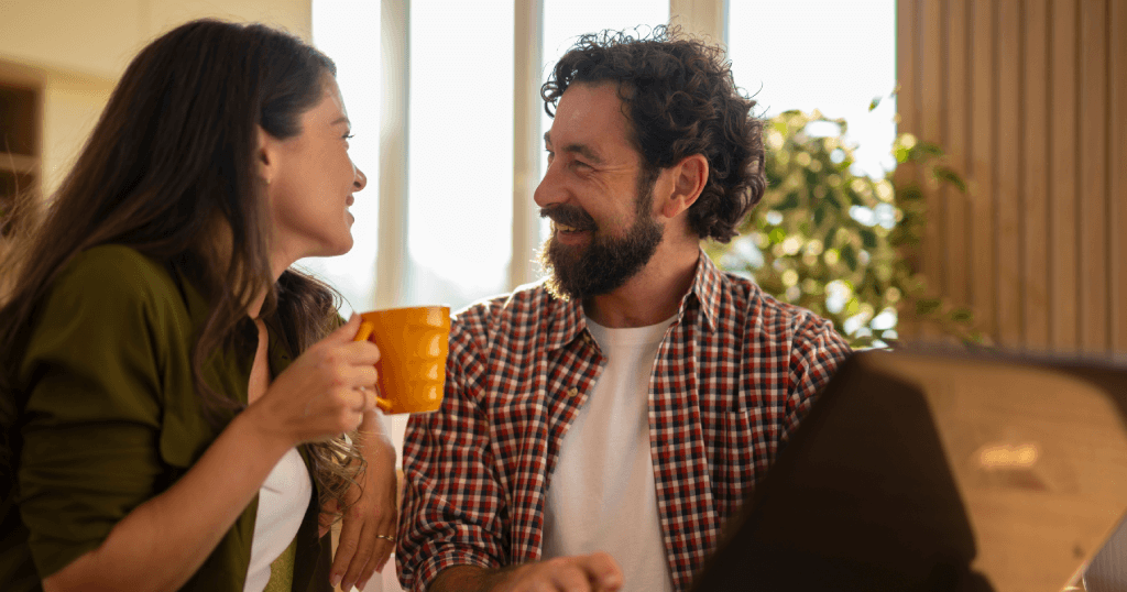 Smiling bearded man looking at his partner holding a yellow mug during a conversation.