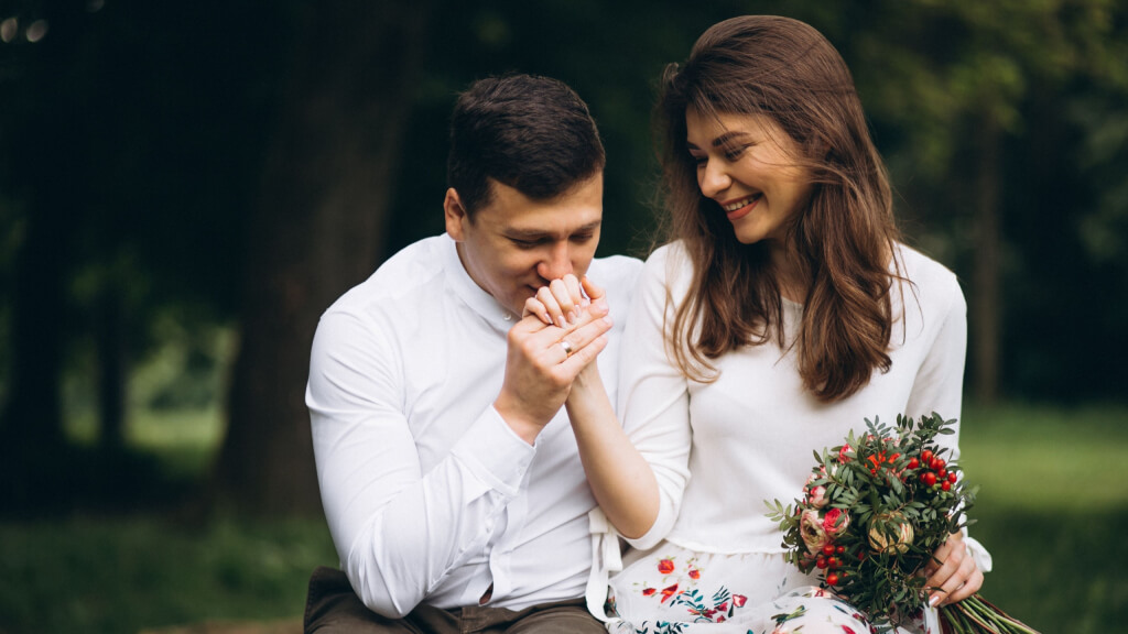 Man gently kissing his partner's hand outdoors while showing affection and emotional connection.