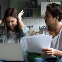 Frustrated woman covering her ears while man holds financial documents during an argument.