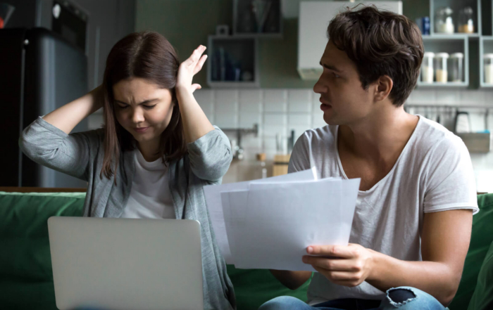Frustrated woman covering her ears while man holds financial documents during an argument.