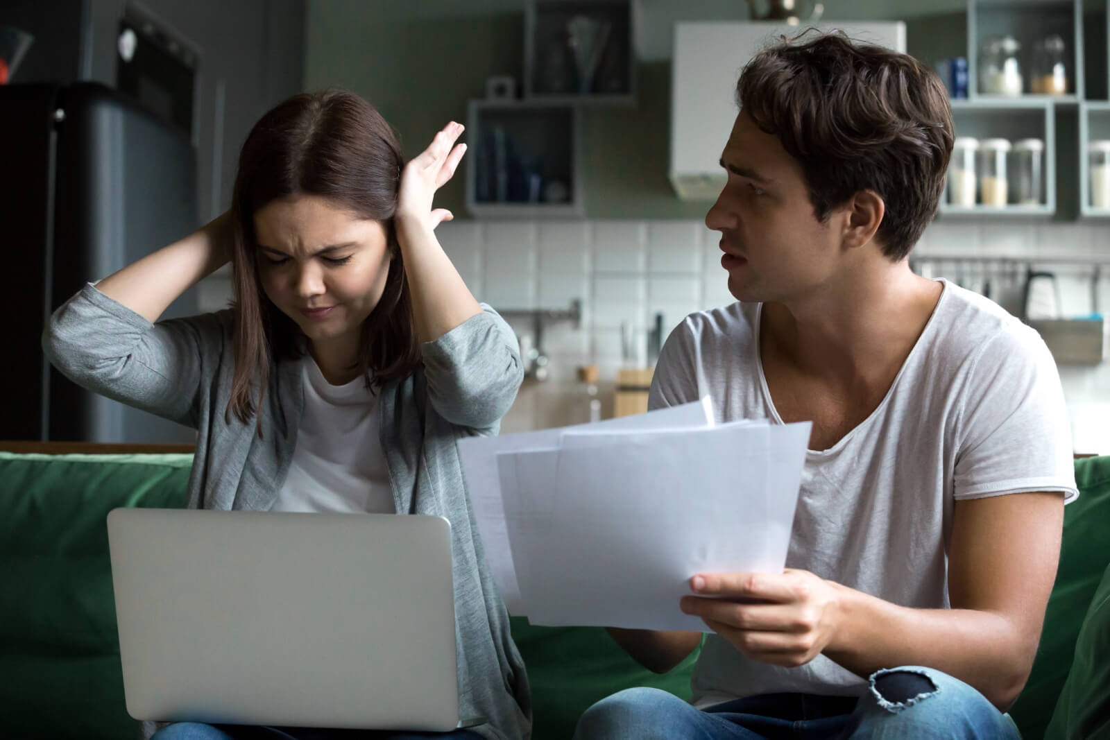 Frustrated woman covering her ears while man holds financial documents during an argument.