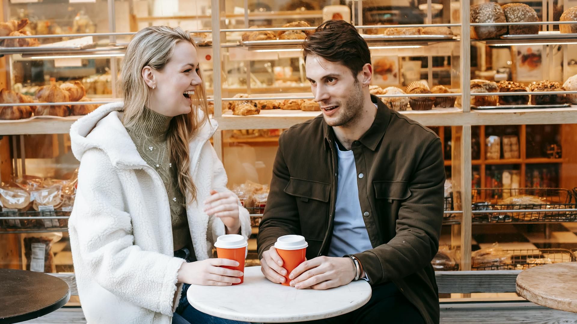 Smiling couple chatting over coffee outside a bakery during a romantic date