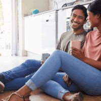 Smiling couple sitting on the floor together, holding coffee mugs and enjoying quality time.