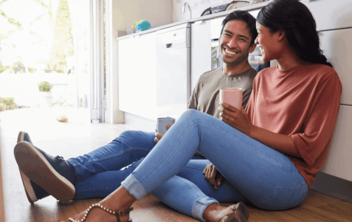 Smiling couple sitting on the floor together, holding coffee mugs and enjoying quality time.
