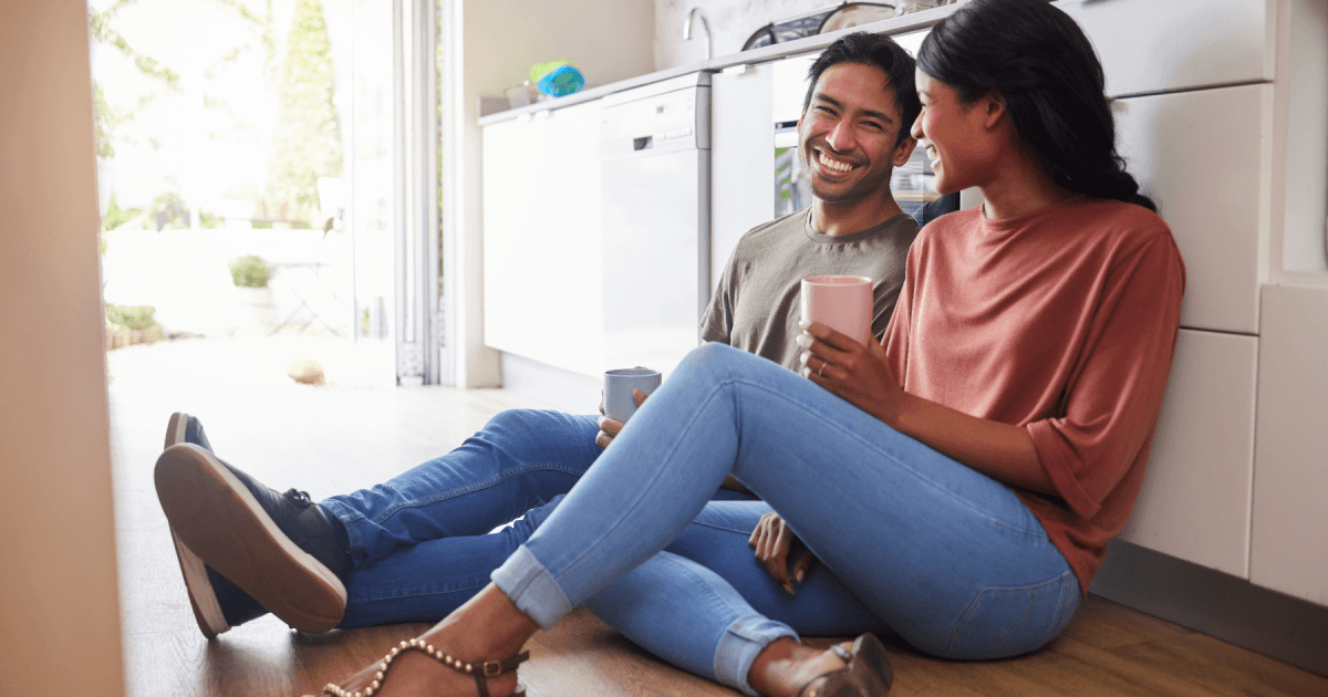 Smiling couple sitting on the floor together, holding coffee mugs and enjoying quality time.