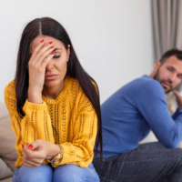 A stressed woman holding her forehead sitting next to an upset man