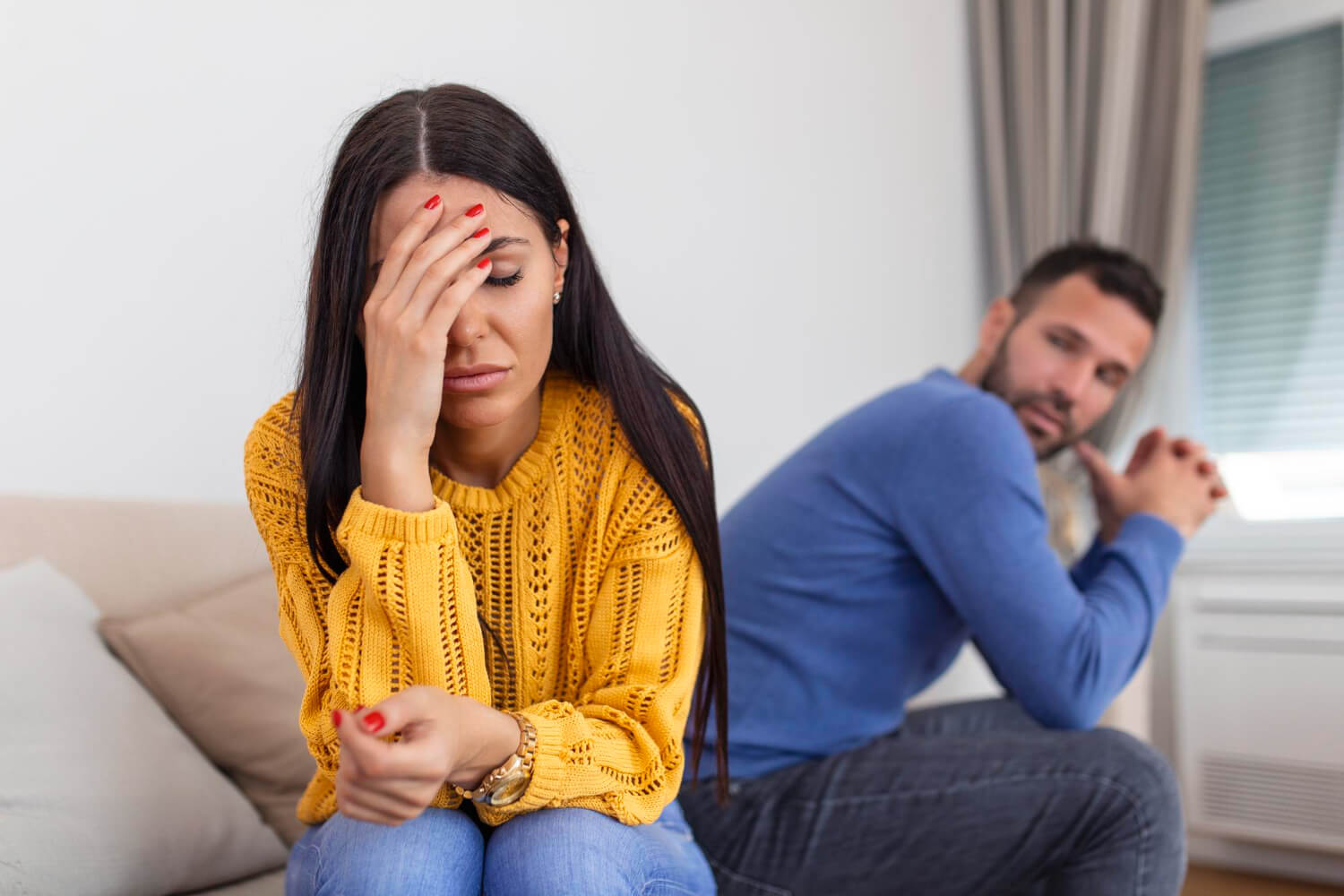 A stressed woman holding her forehead sitting next to an upset man