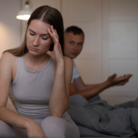 A woman resting her head in hand feeling stressed while her partner sits in the background