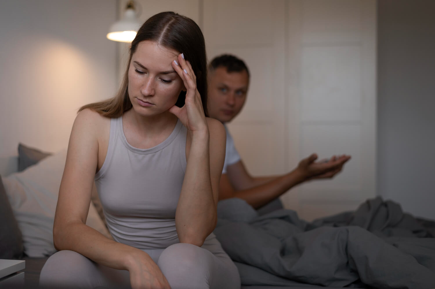 A woman resting her head in hand feeling stressed while her partner sits in the background