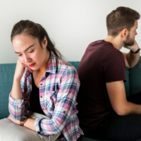A frustrated couple sitting back-to-back on a sofa in deep thought