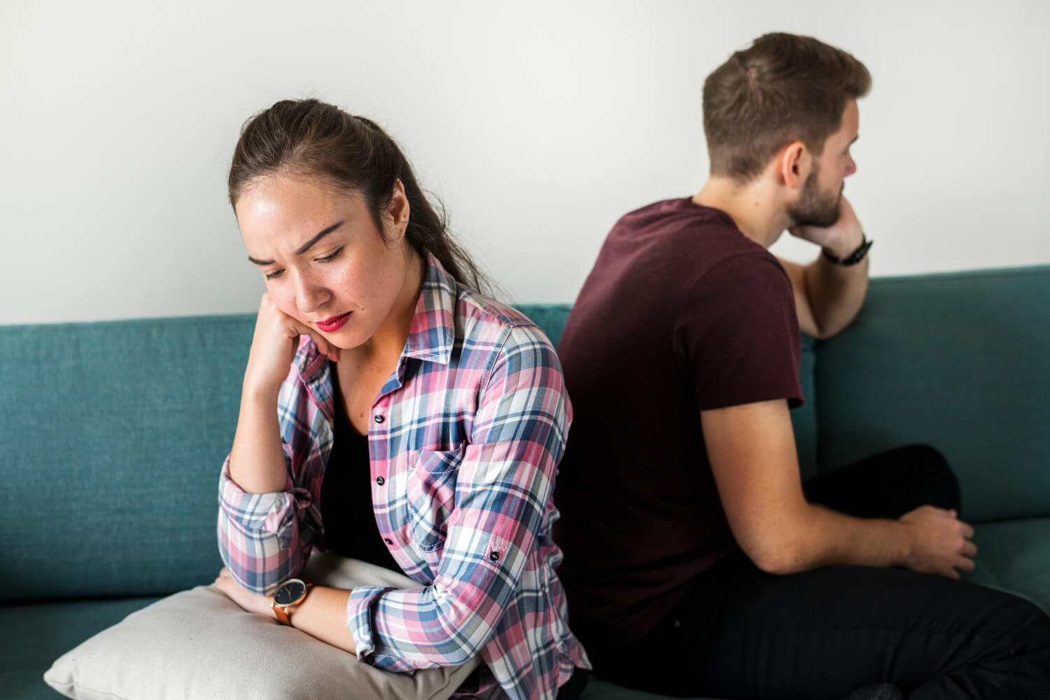 A frustrated couple sitting back-to-back on a sofa in deep thought