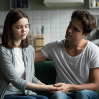 Man holding his partner's hand to comfort her during a serious conversation at home.