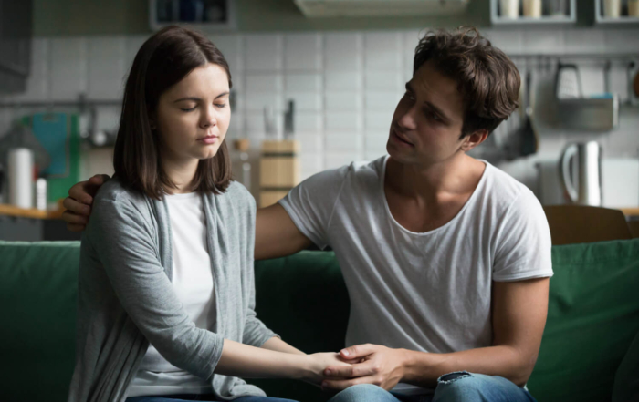 Man holding his partner's hand to comfort her during a serious conversation at home.