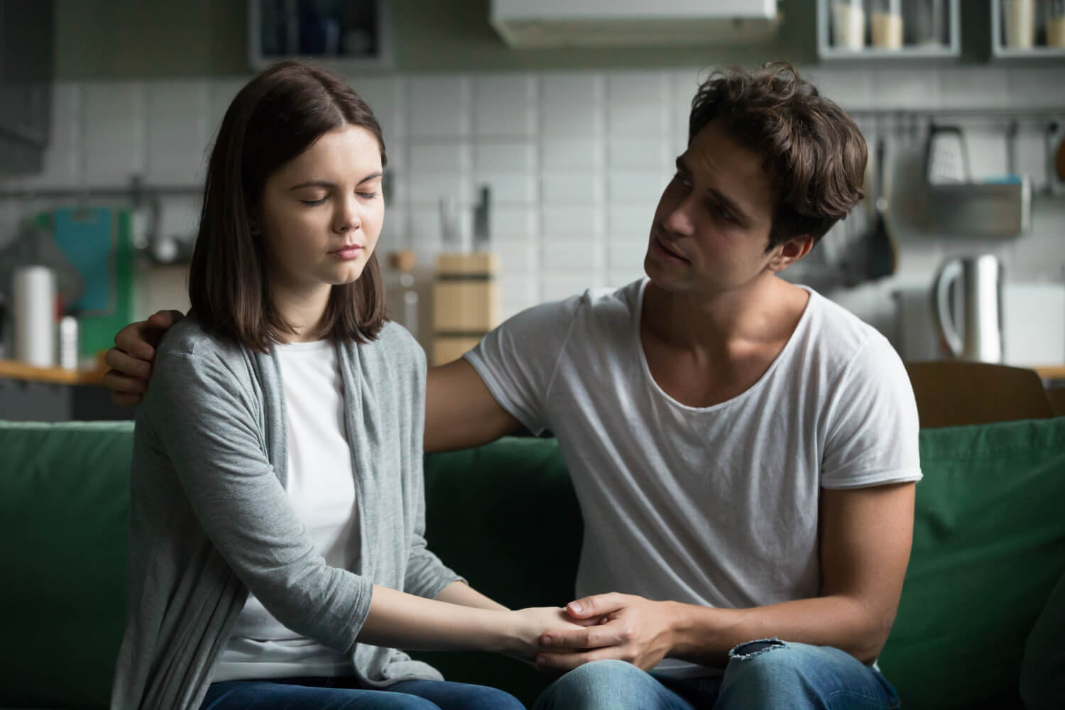 Man holding his partner's hand to comfort her during a serious conversation at home.